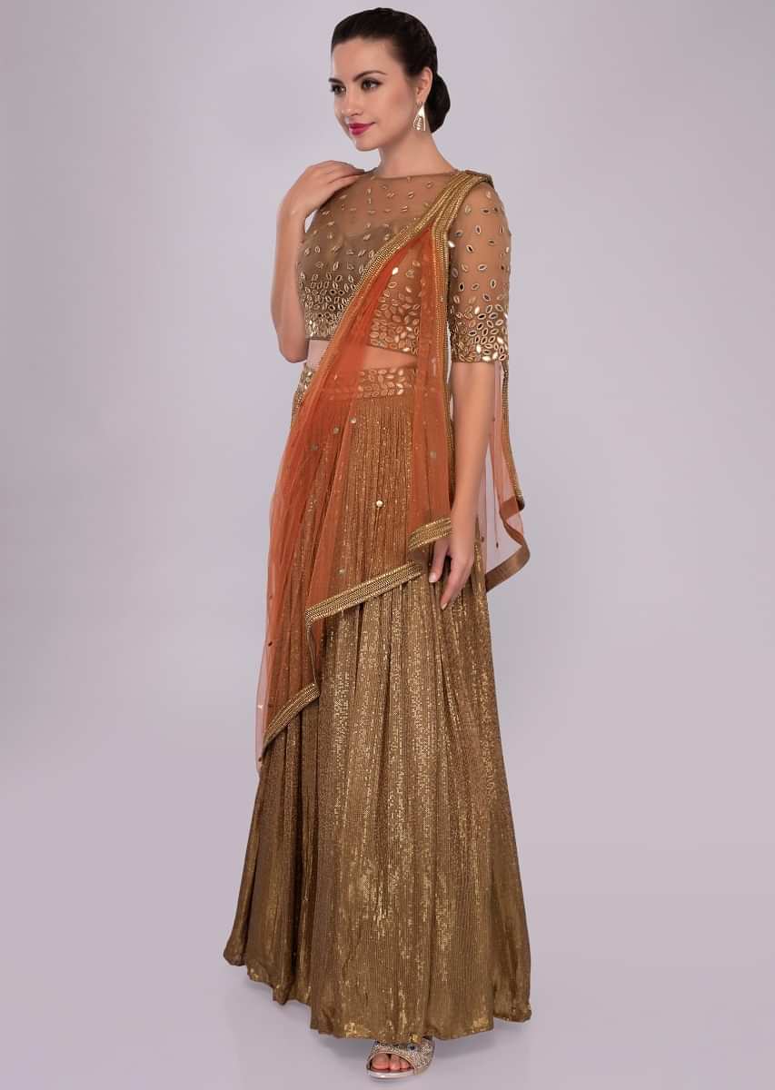 Fancy fabric lehenga paired with embroidered net blouse and contrasting orange dupatta 