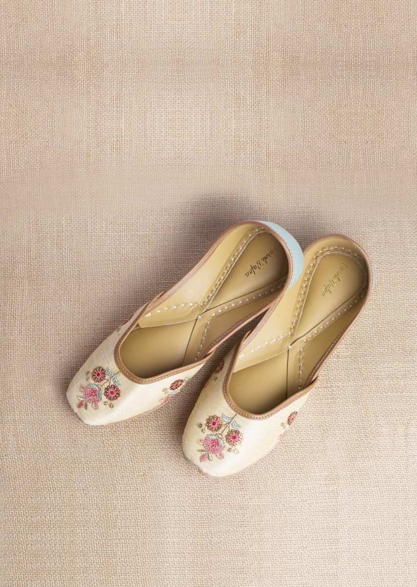 Light Gold Juttis In Raw Silk With Embroidered Multicolored Floral Motifs Using Sequins And Resham Work By Vareli Bafna