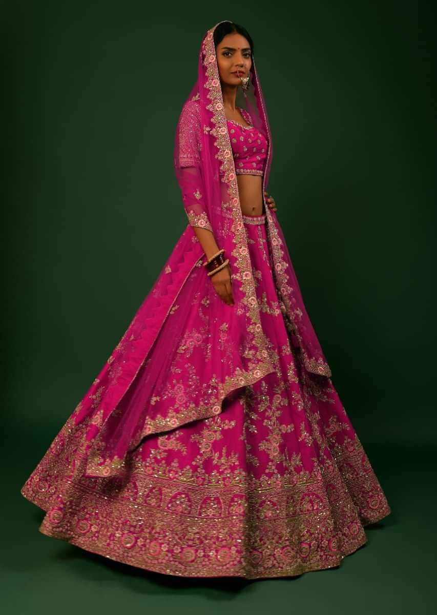 Rani Pink Lehenga Choli In Raw Silk With Golden Zari Embroidered Heavy Mughal Border And Floral Jaal With Colorful Resham Flowers 